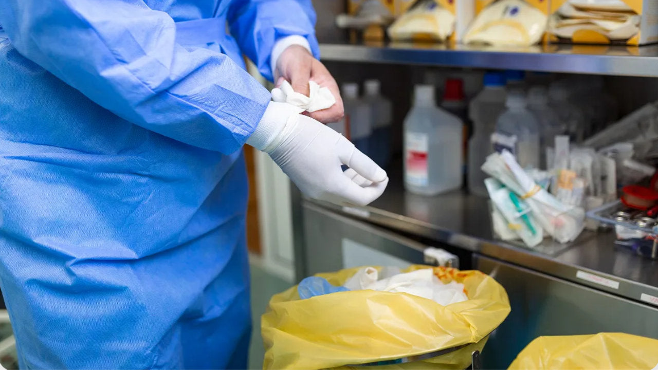 Professionnel de santé en surblouse tenant une compresse au-dessus d'un sac DASRI jaune